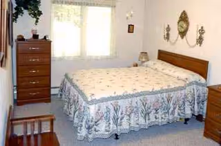 A furnished bedroom with a large bed, dresser, and window in a retirement community.