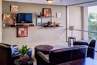 A lounge area with black leather seating, small tables, plants, and a wall-mounted TV.