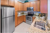 Corner kitchen featuring a stainless steel refrigerator and range with built-in microwave, granite countertops, wooden cabinets, and a double sink.