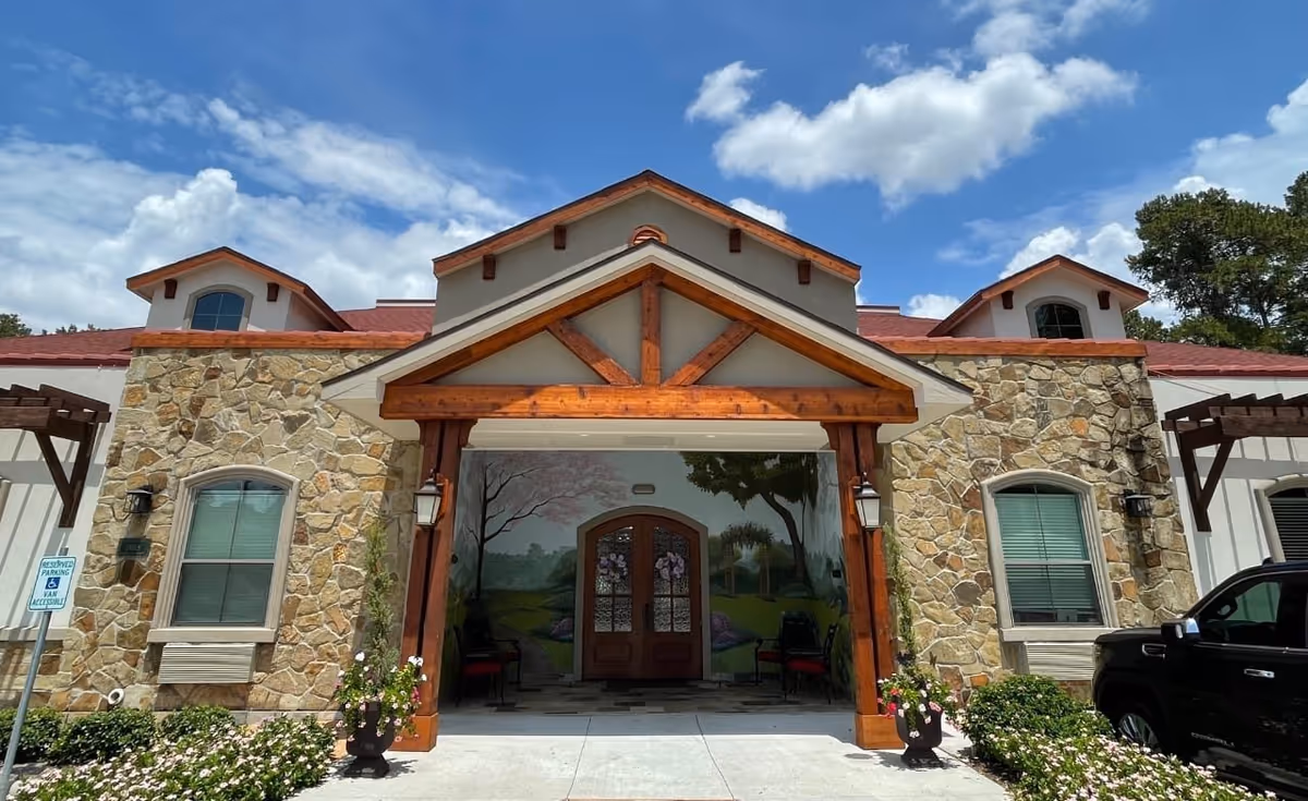Front view of a stone-and-wood entrance at Village Green Memory Care Community Cypress Louetta