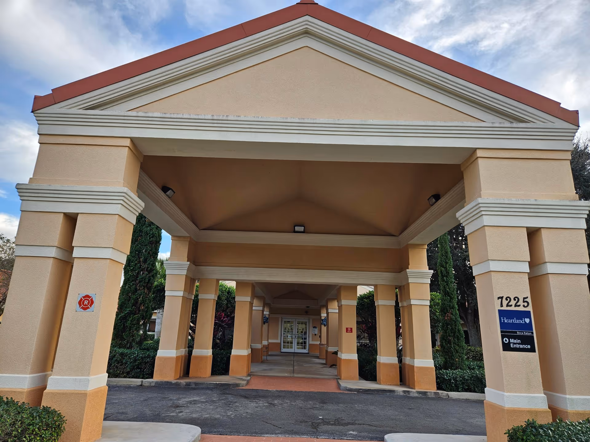 Covered portico entrance with columns leading to the main glass doors and a sign reading 7225 Heartland Main Entrance.