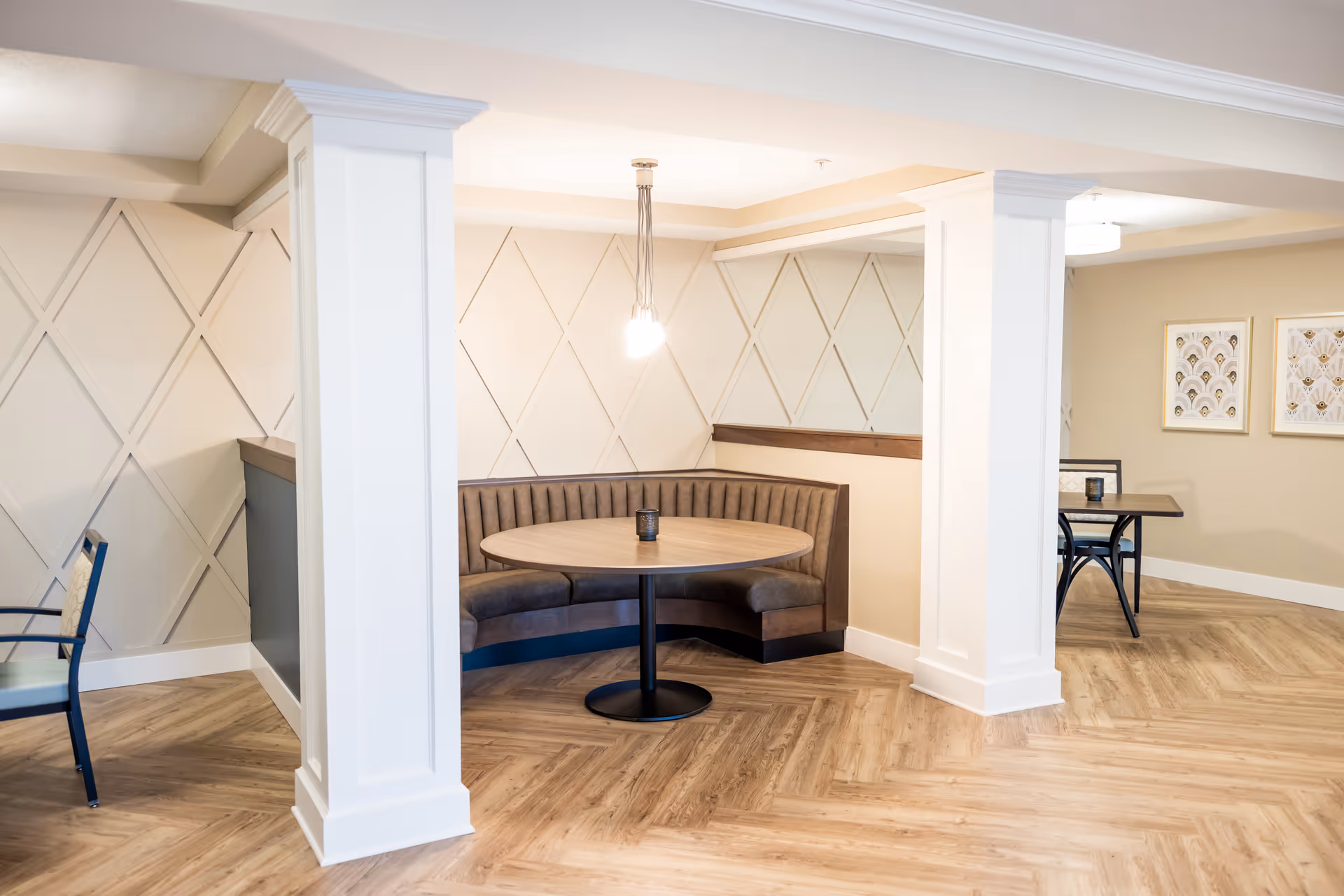 Light-filled dining nook with a round table and curved banquette seating in a senior living common area.
