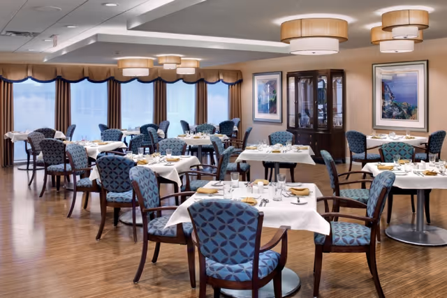 Spacious dining room with neatly set tables and blue patterned chairs under pendant lights.