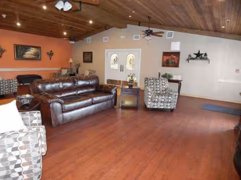 Cozy lounge area with brown leather sofa, patterned chairs, and wooden ceiling in a senior facility.