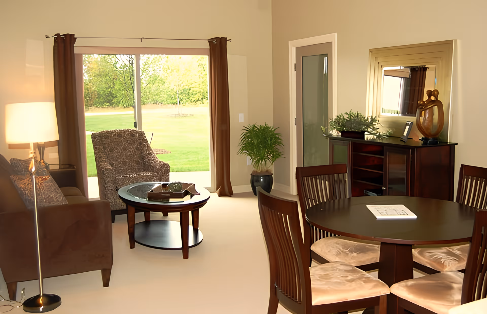 Cozy combined living and dining area with a round dining table and chairs, sofa and armchair around a coffee table, and a sliding glass door opening to a grassy yard.