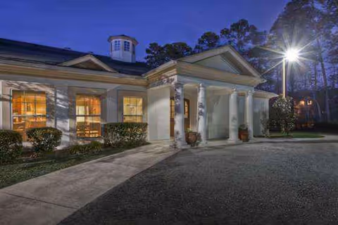 Exterior view of a senior living facility entrance with columns and warm interior lights.