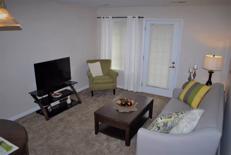 Cozy living room with a sofa, armchair, coffee table, TV on a stand, and a door with blinds.