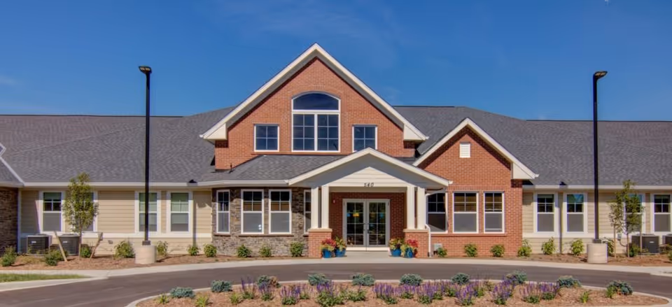 A brick senior living facility with a central covered entrance and landscaped front.