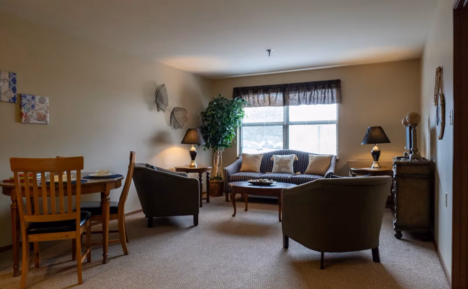 Living room with a sofa and two armchairs around a coffee table, side lamps, a potted plant, and a small dining table near the wall.