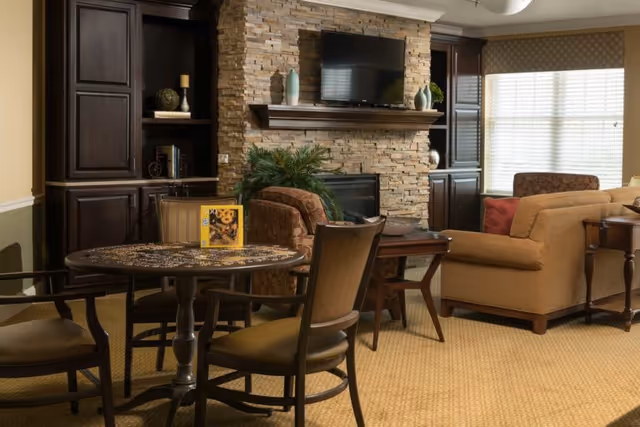 Cozy living room with a round table and chairs, stone fireplace with a mounted TV, sofas and built-in cabinets.