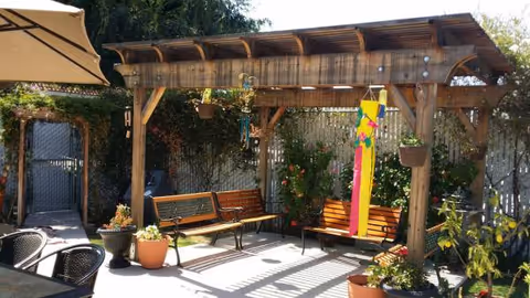 Outdoor courtyard with a wooden pergola, benches, and potted plants.