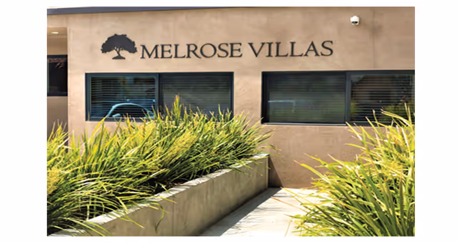 Front exterior of Melrose Villas with a walkway, plants, and large windows.