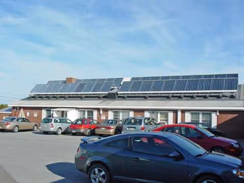 Single-story brick building with solar panels, parked cars in the front lot under a blue sky.