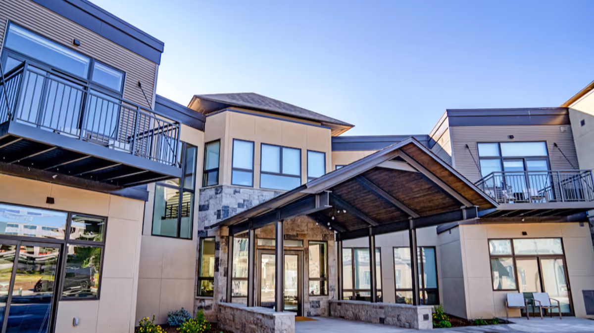 Front entrance of a modern senior living building with a covered entryway, stone accents and balconies.