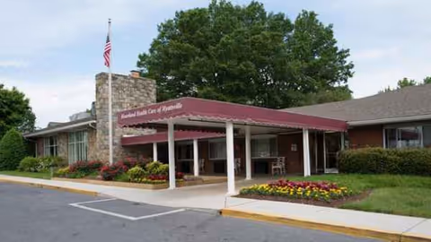 Front entrance of a Hyattsville senior living facility with a maroon canopy and manicured flower beds.