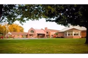 Brick senior care center building with a large grassy lawn and trees in the foreground.