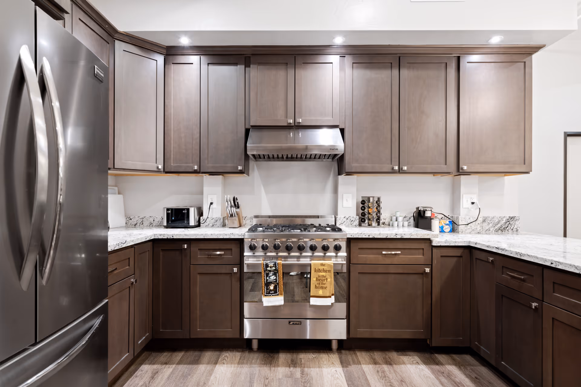 Modern kitchen with dark wood cabinets, stainless steel refrigerator and stove, granite countertops, a microwave, knife block, coffee maker, and spice rack.