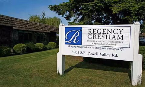 A white Regency Gresham Nursing & Rehab Center sign sits on a grassy lawn.