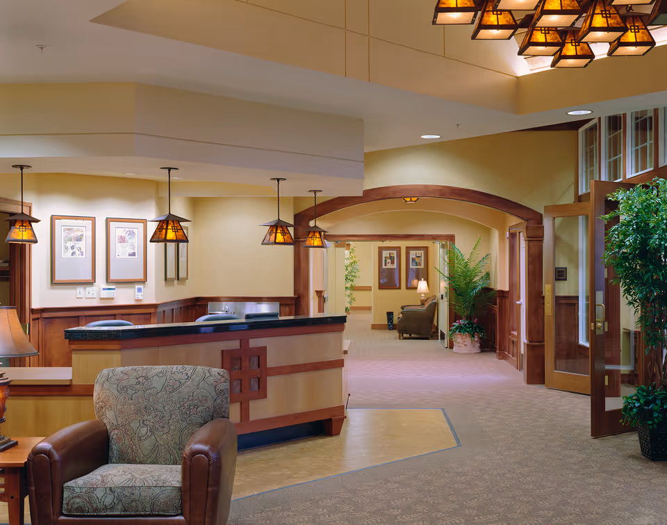 Reception lobby with a front desk, pendant lights, upholstered chairs, and a decorative archway leading to a seating area.