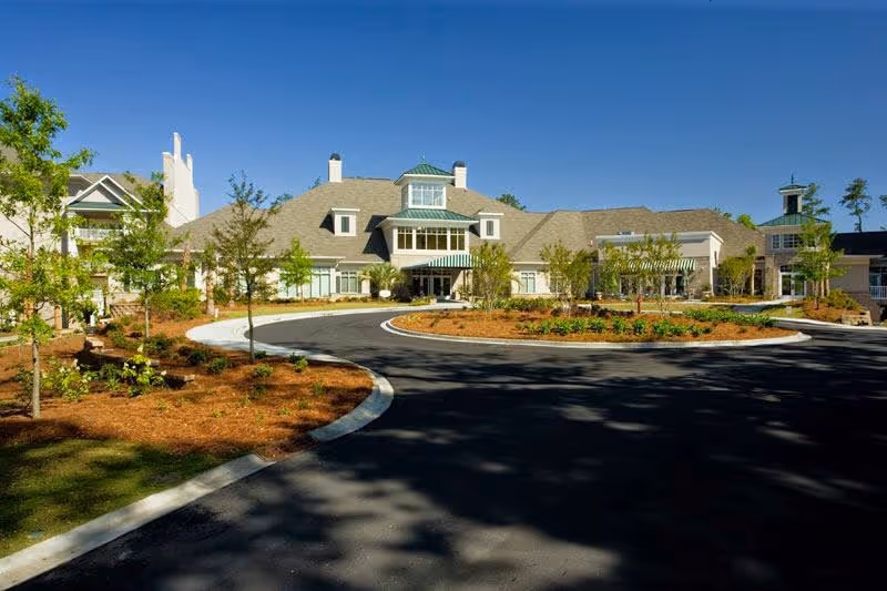 Exterior view of a large, single-story building with a circular driveway and landscaped garden beds in front, under a clear blue sky.