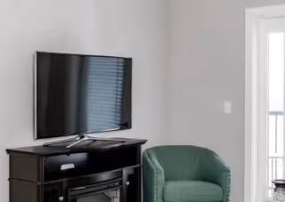 Small living area with a wall-mounted TV above a black console and a green armchair near a glass door.