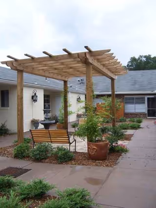 Wooden pergola over a courtyard with a bench and potted plants.