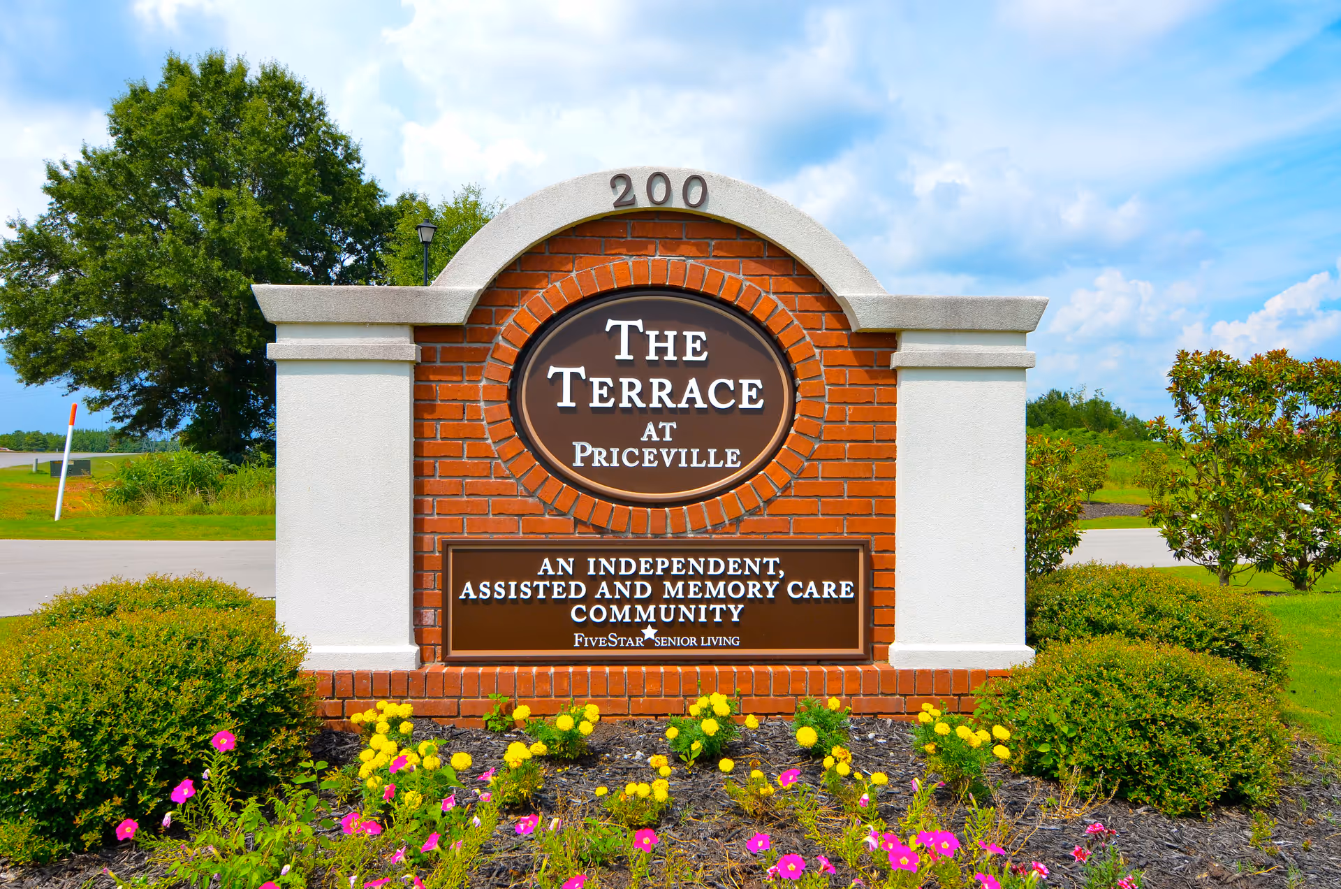 Brick and stone entrance sign reading 'The Terrace at Priceville' surrounded by shrubs and flowers under a blue sky.
