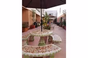 Outdoor courtyard with mosaic circular bench seating around a central table and umbrella between single-story buildings.