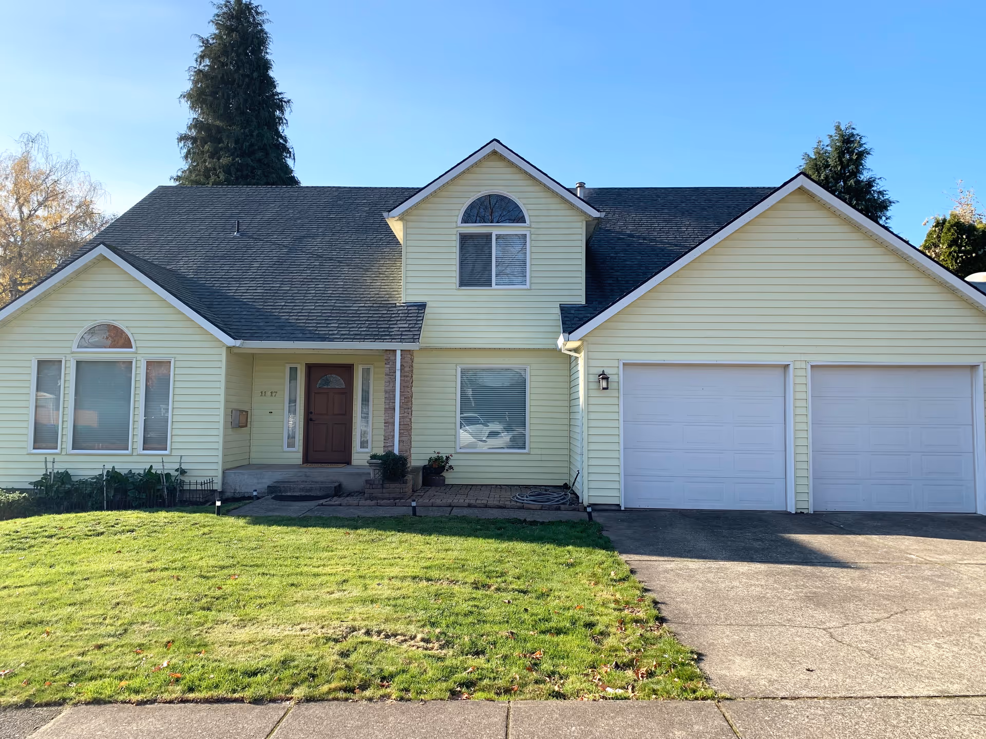 Front exterior of a pale yellow two-story house with a double garage, front lawn, and driveway.