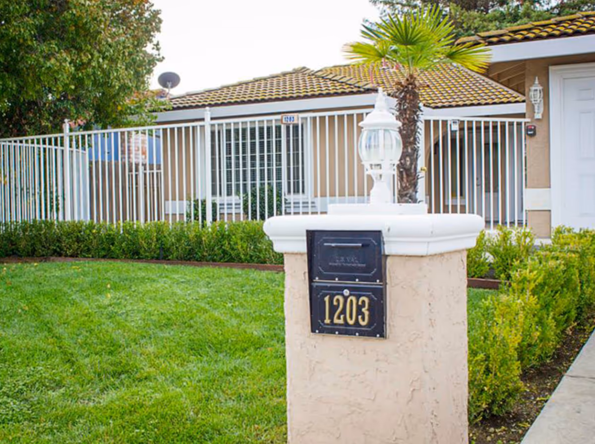Front yard and gated entrance of a single-story house with a mailbox post numbered 1203.