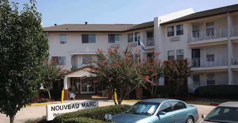 Exterior view of a two-story senior living building with a sign and parked cars
