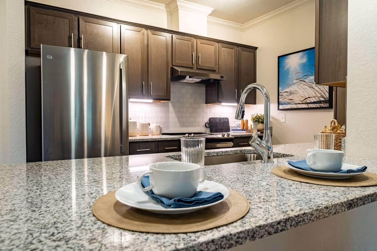 Kitchen with a granite breakfast bar set for two, stainless steel appliances, dark wood cabinets and a chrome faucet.