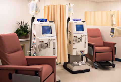 A medical treatment room with two dialysis machines and red recliner chairs.