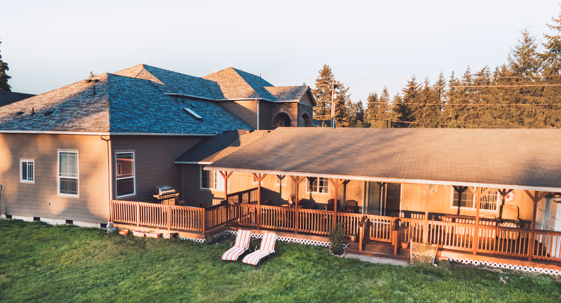 Exterior view of a residential care building with a covered wooden porch, grassy lawn, and two striped lounge chairs.