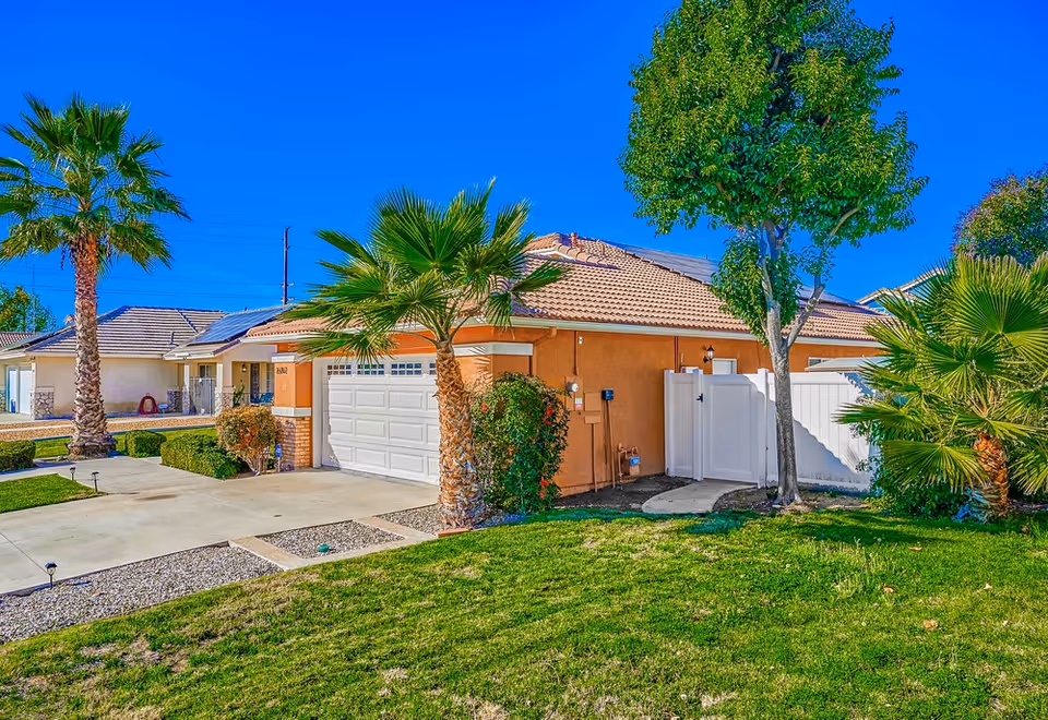 Front view of a peach-colored, single-story assisted living home with a white garage and palm trees.