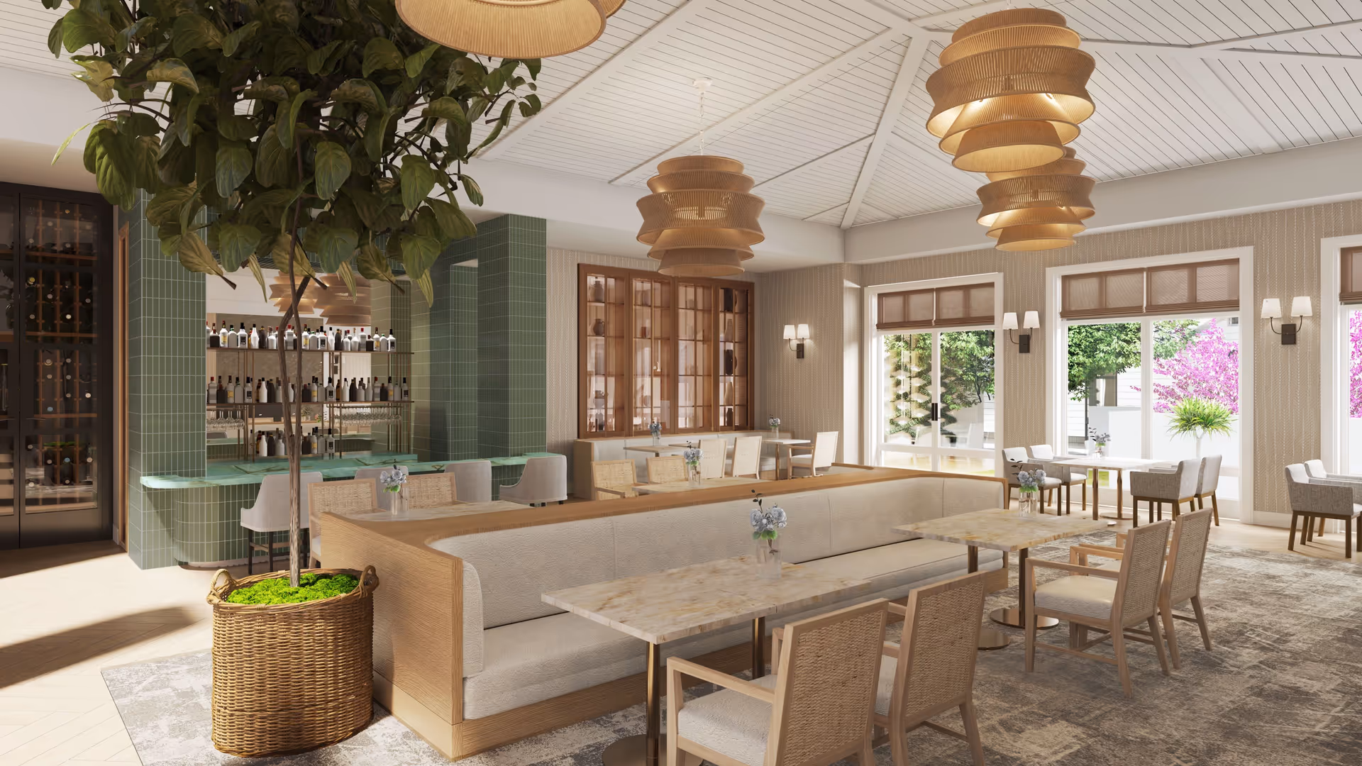 A spacious and well-lit dining area with multiple tables and chairs arranged for seating. The room features large windows allowing natural light to brighten the space, with views of greenery and flowering plants outside. There are modern pendant lights hanging from the ceiling, a large potted plant in a wicker basket, and a bar area with bottles and glassware displayed behind a green-tiled counter.