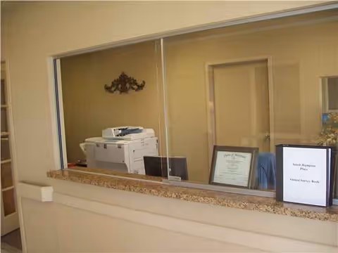 Reception area behind a glass window with a printer and framed documents on the counter
