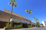 Exterior view of North Mountain Medical And Rehabilitation Center building with a clear blue sky, several tall palm trees, and parked cars along the driveway.