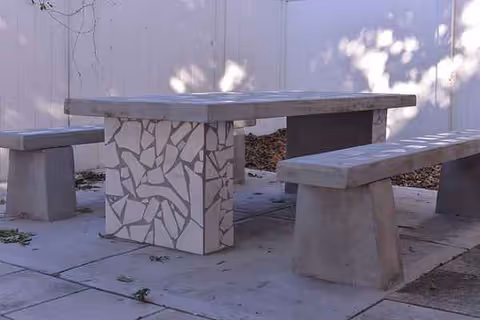 Concrete table with mosaic base and two benches outside a building.