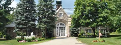 Stone building with arched entrance, surrounded by trees and a gravel path.