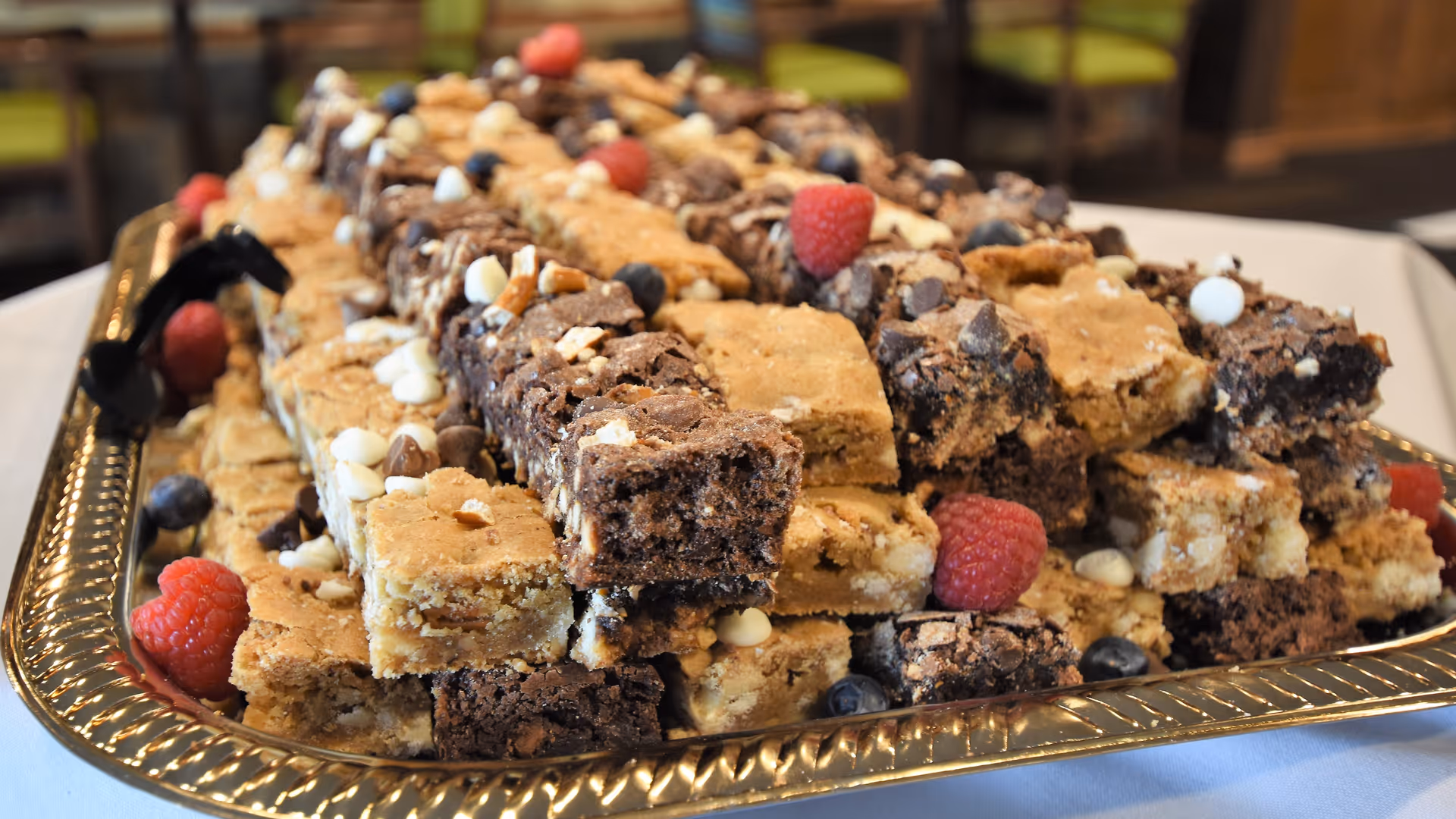 A large gold tray piled with chocolate brownie and blondie squares garnished with raspberries and blueberries.