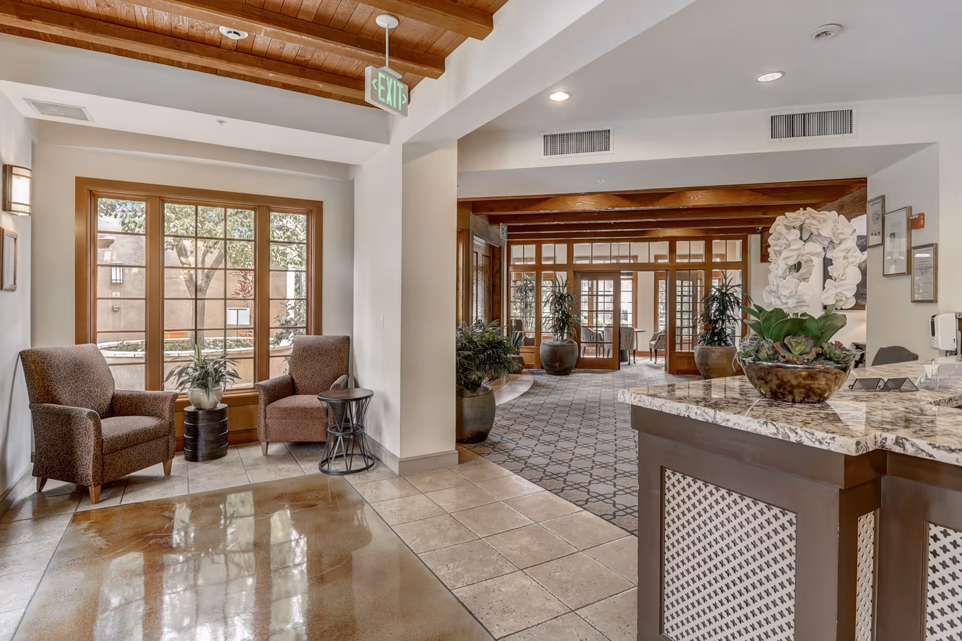 Bright reception lobby with two armchairs by a window, potted plants, and a marble-topped front desk.