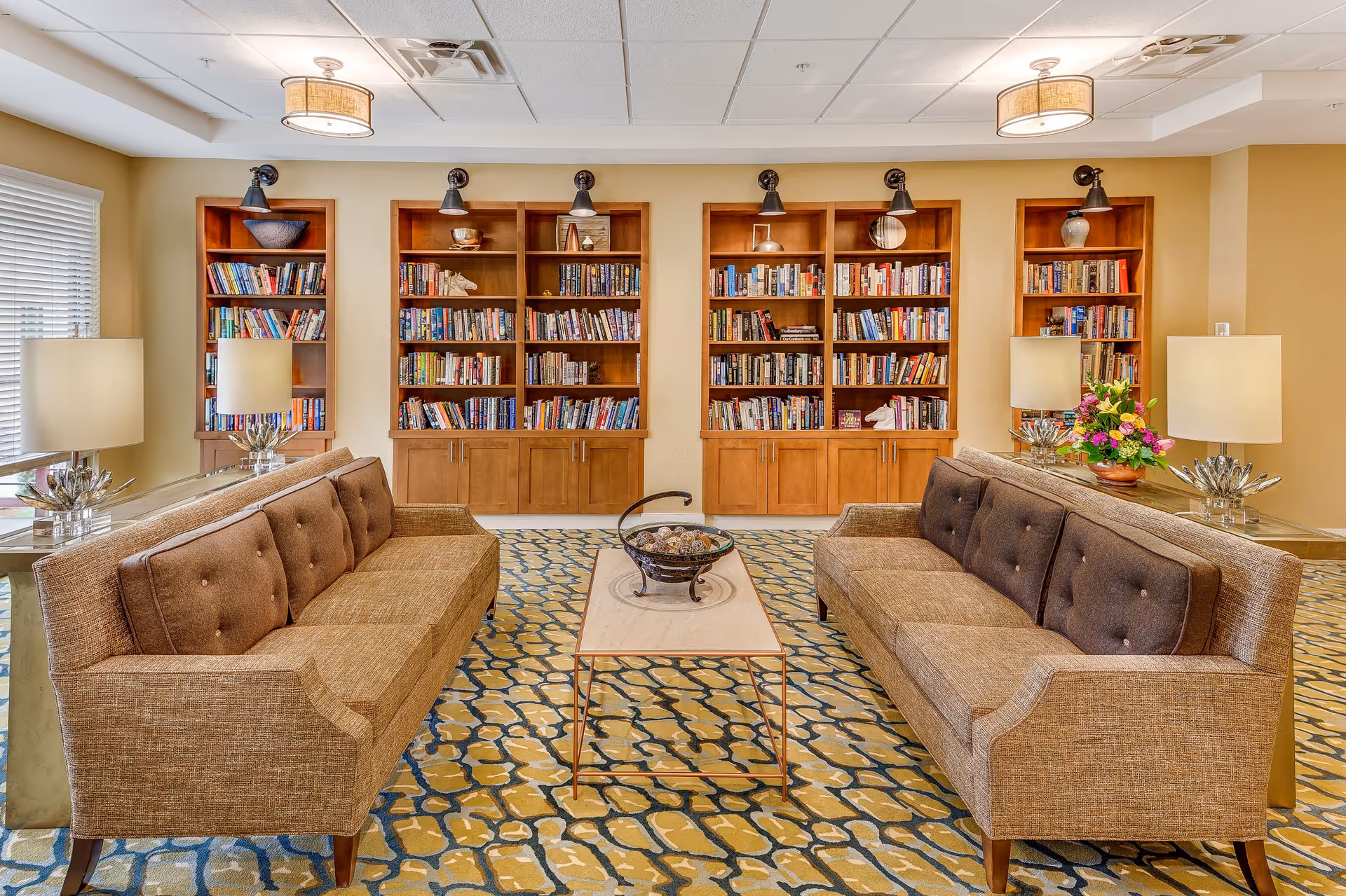 A cozy common room with two facing sofas, a central coffee table, and built-in bookshelves filled with books.