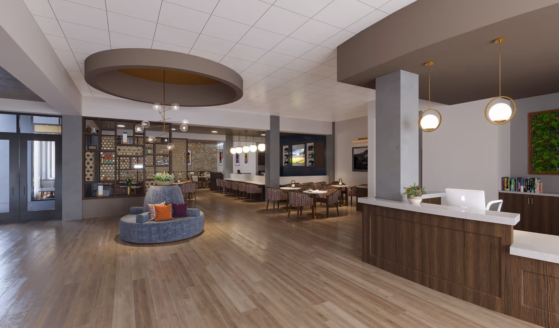 Spacious and modern senior living facility common area with wooden flooring, a circular seating arrangement with colorful cushions in the center, a reception desk with a computer and potted plant, multiple dining tables with chairs, pendant lighting, and decorative wall art including a green plant frame and a wine rack.
