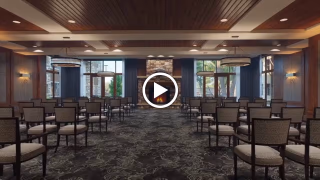 Large elegant multipurpose meeting room with rows of chairs facing a stone fireplace and large windows.