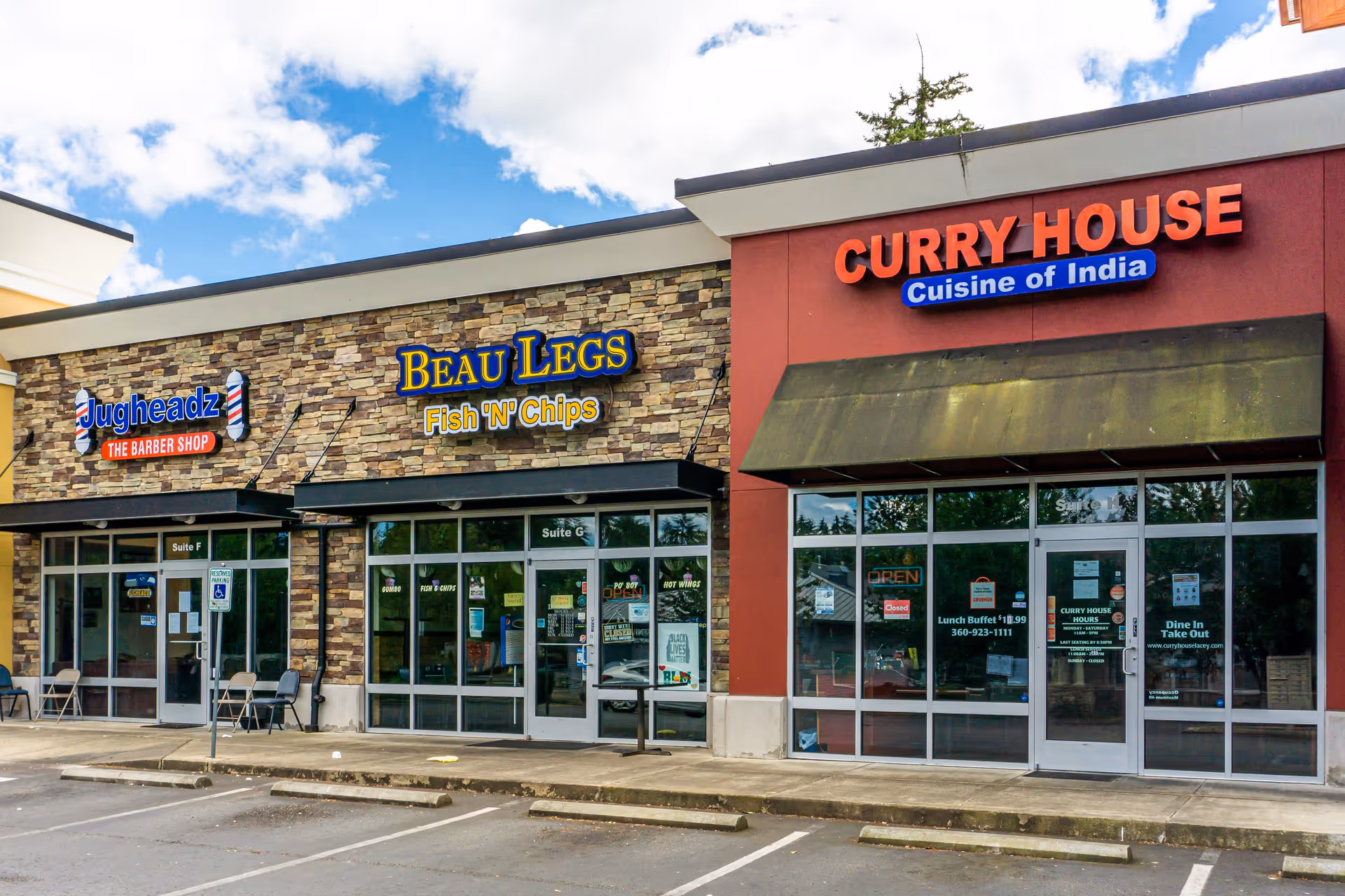 Strip-mall storefronts including Beau Legs Fish 'N' Chips and Curry House with empty parking spaces in front under a partly cloudy sky.
