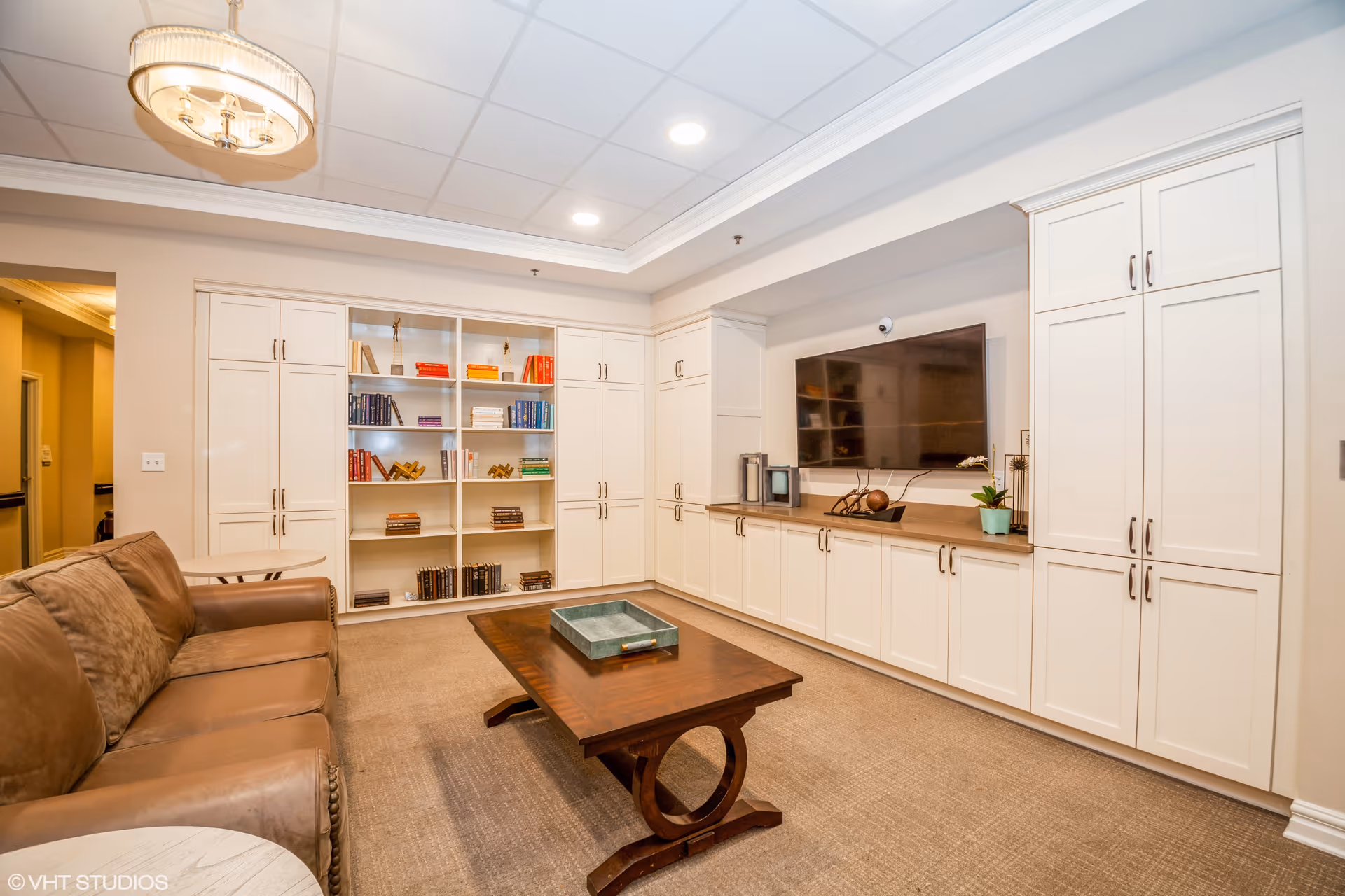 Cozy sitting room with a leather sofa, wooden coffee table, built-in white cabinets and bookshelves, and a wall-mounted TV.