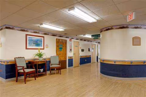 Interior hallway of a senior living facility with seating area and wooden doors.