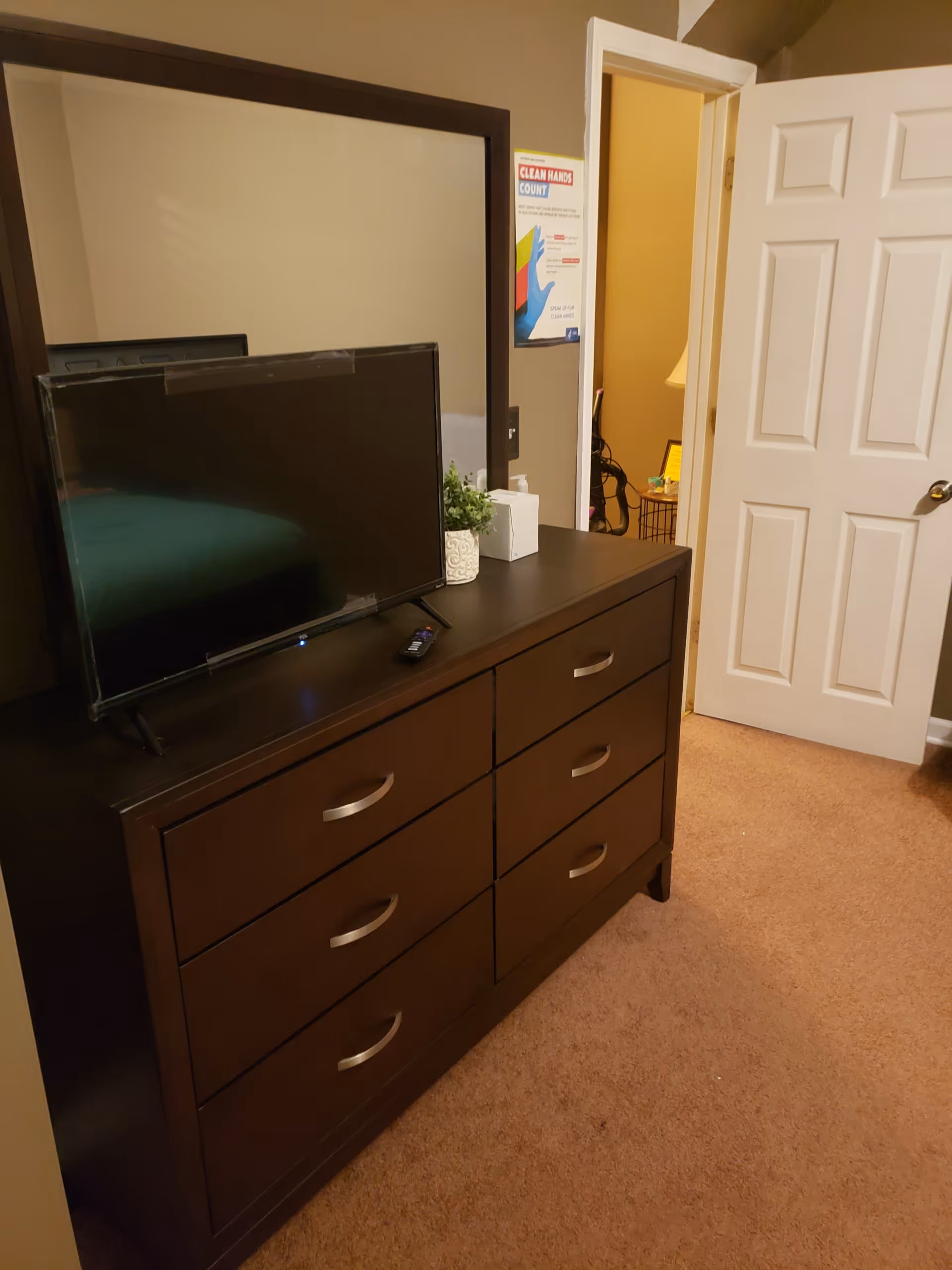 Dark wood dresser with a mirror and a TV on top in a bedroom, with an open door leading to a hallway.