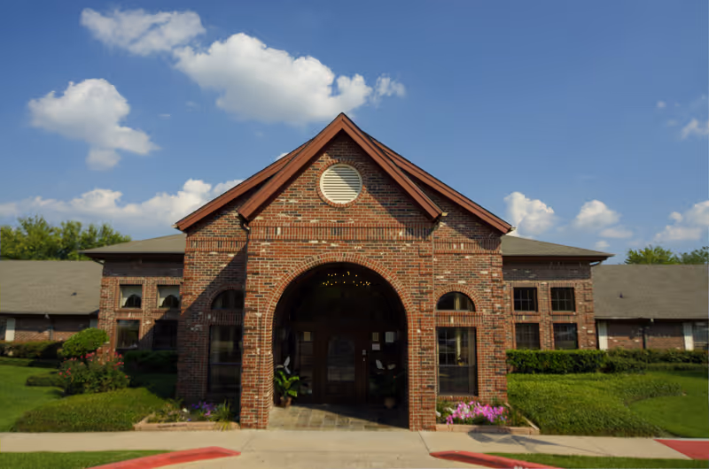 Brick single-story building entrance with an arched doorway and gabled roof under a blue sky.